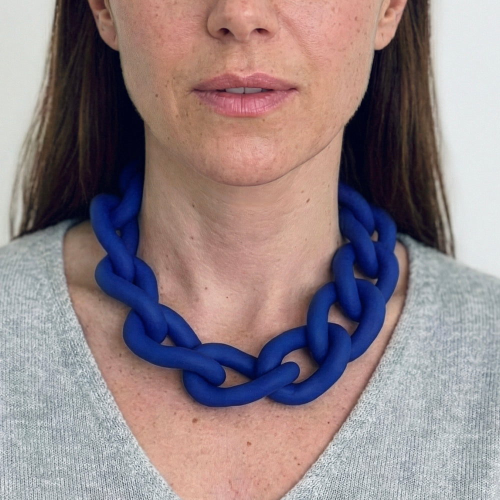 Woman wearing a bold blue statement necklace to show the large architectural links and lightweight fit. Contemporary jewellery design.