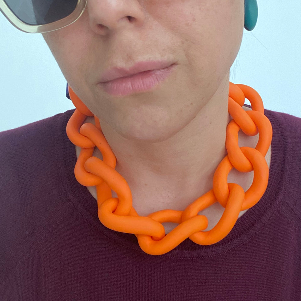 Woman wearing a bold orange statement necklace to show the large architectural links and lightweight fit. Contemporary jewellery design.