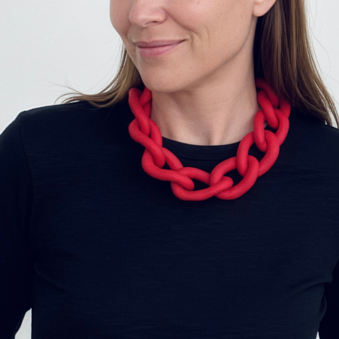 Woman wearing a bold red statement necklace to show the large architectural links and lightweight fit. Contemporary jewellery design.