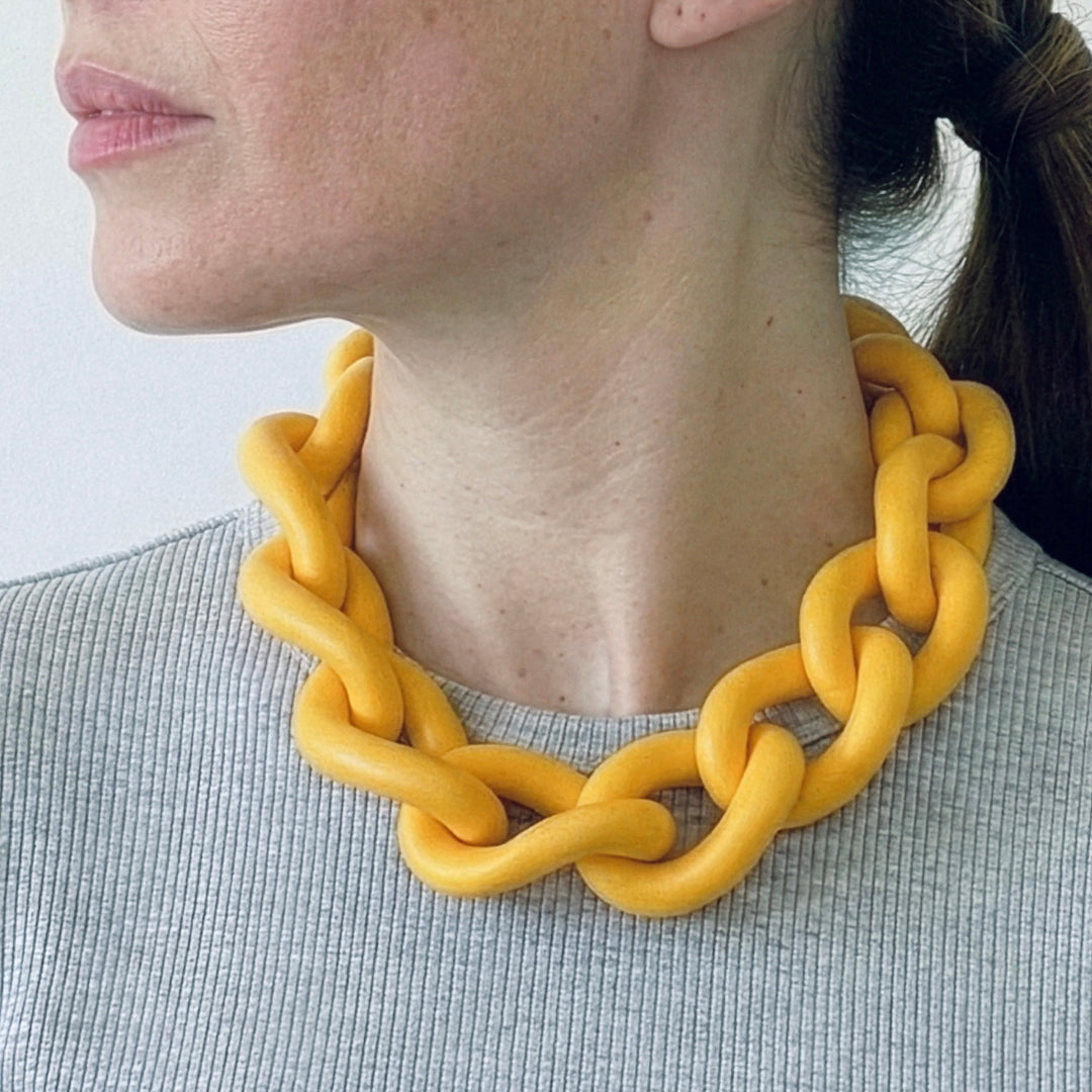 Woman wearing a bold yellow statement necklace to show the large architectural links and lightweight fit. Contemporary jewellery design.