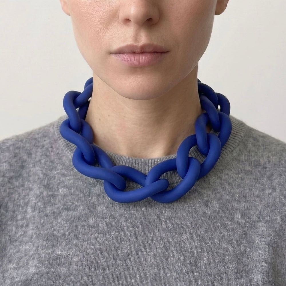 Woman wearing a bold blue statement necklace to show the large architectural links and lightweight fit. Contemporary jewellery design.