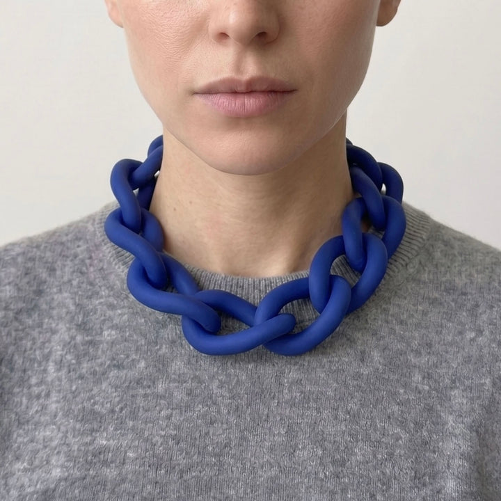 Woman wearing a bold blue statement necklace to show the large architectural links and lightweight fit. Contemporary jewellery design.