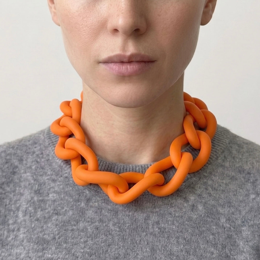 Woman wearing a bold orange statement necklace to show the large architectural links and lightweight fit. Contemporary jewellery design.