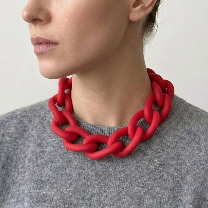 Woman wearing a bold red statement necklace to show the large architectural links and lightweight fit. Contemporary jewellery design.