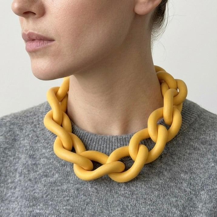Woman wearing a bold yellow statement necklace to show the large architectural links and lightweight fit. Contemporary jewellery design.